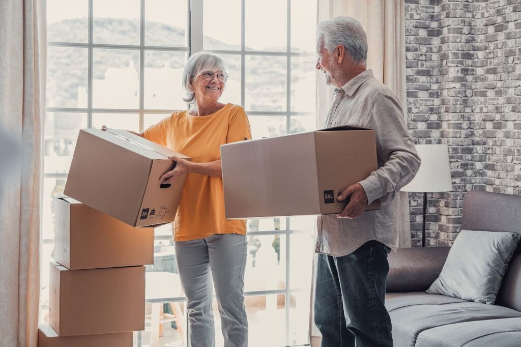 an elderly couple holding moving boxes