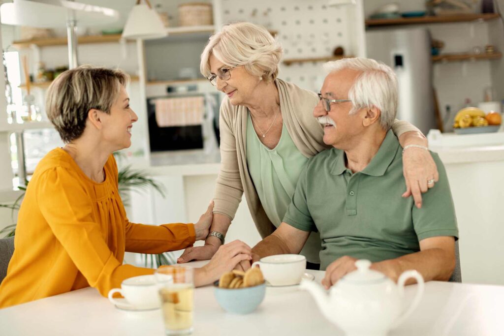 A woman sits happily at the kitchen table with her elderly parents.