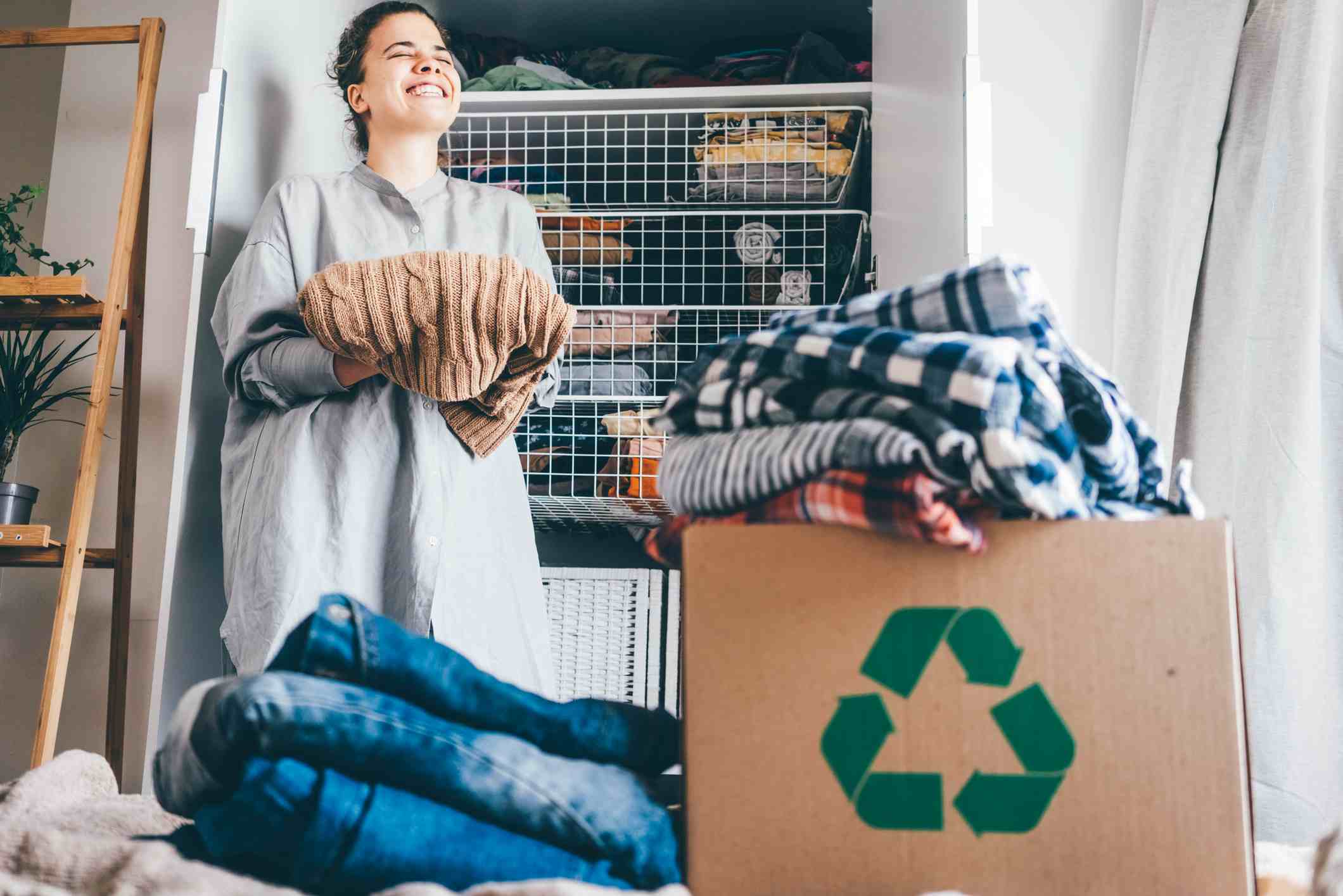 iStock-1327937157 Recycle clothes concept. Young woman with recycling box full clothes.