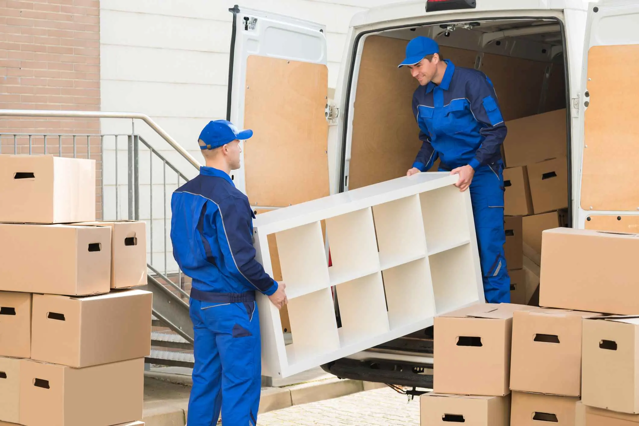 Young male movers unloading furniture and cardboard boxes from truck on street