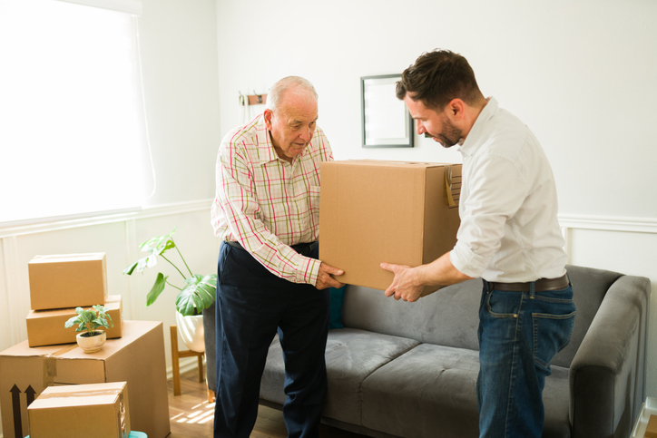 Elderly man moving into a new apartment with the help of his son Young man carrying boxes and helping his elderly caucasian father to move to a new apartment