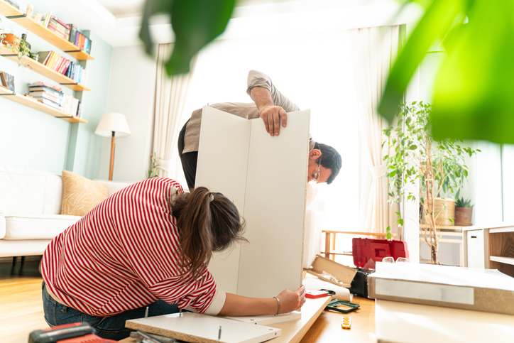 Happy Couple Assembles Furniture as a Team, Girl Reads Instructions and Boy Tightens Screw with a Drill. Moving into New Apartment, Couple Assemble Shelf. Young couple just married assembling a piece of furniture in their home. With screwdriver and tools in hand to follow the instruction book. Handyman couple. They are the owner.New house, new furniture