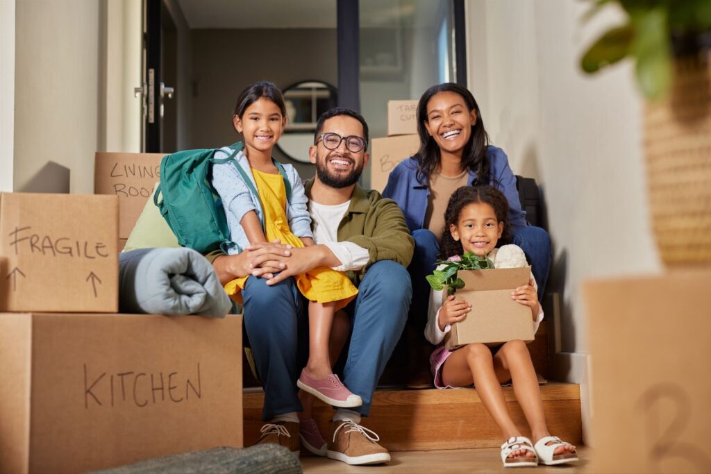 Two parents and their two kids sit together amid packed boxes.