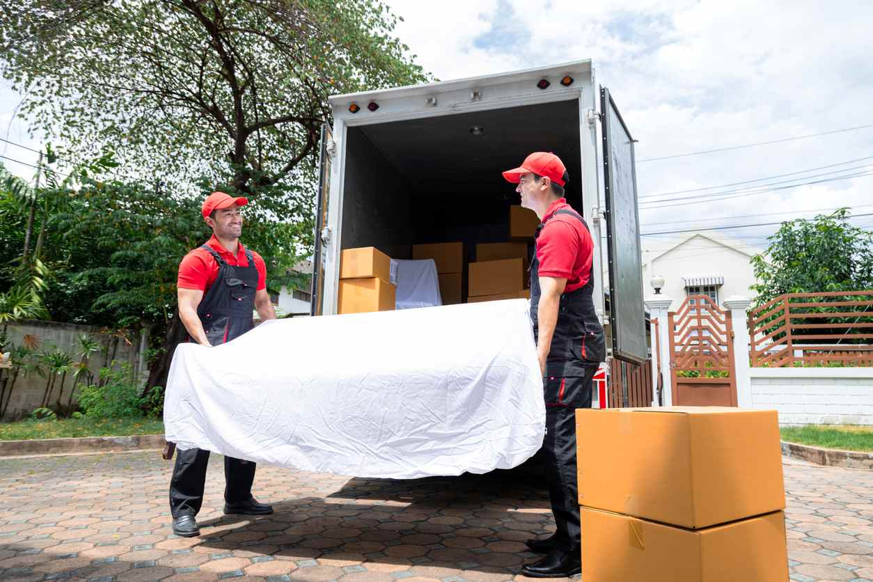 Two moving men carrying a couch out of a moving van.