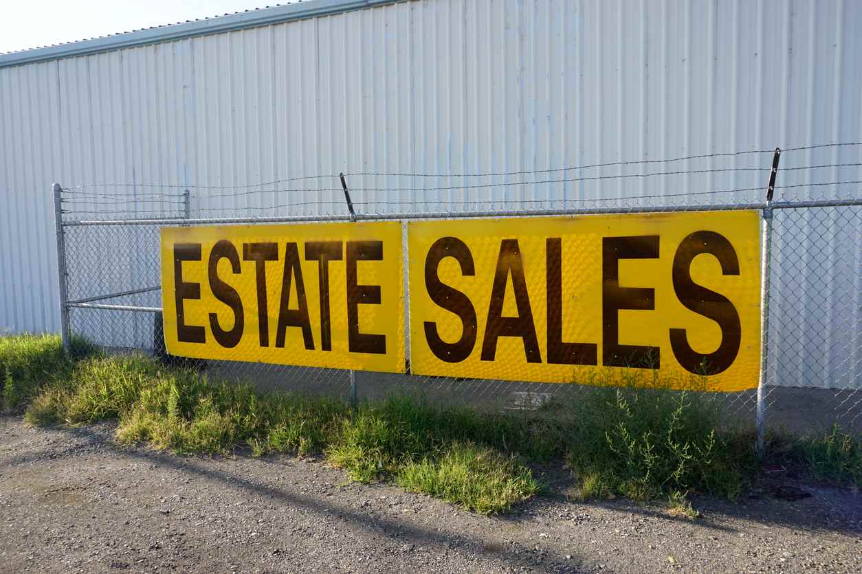 A giant "Estate Sales" sign sits n a chain link fence.