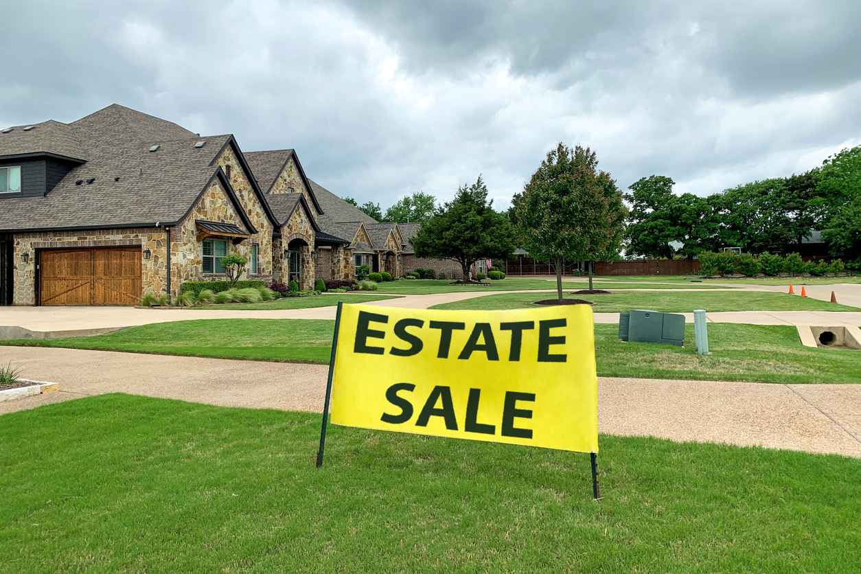 A wide shot of a house featuring an "estate sale" sign in front.