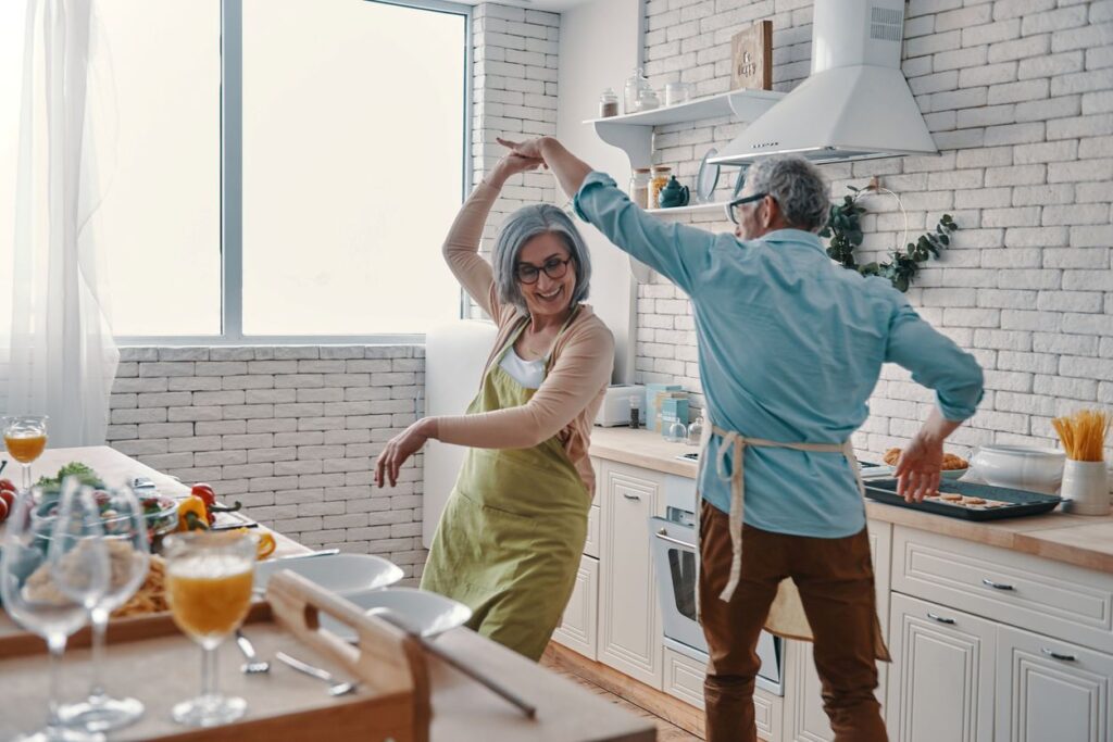 A happy couple dances together while cooking in the kitchen of their well-designed new home.