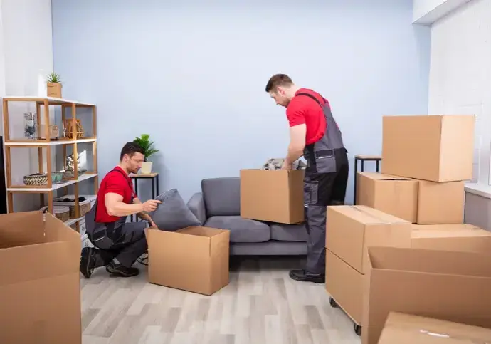 Two Young Movers In Uniform Picking And Putting Products In The Cardboard Boxes