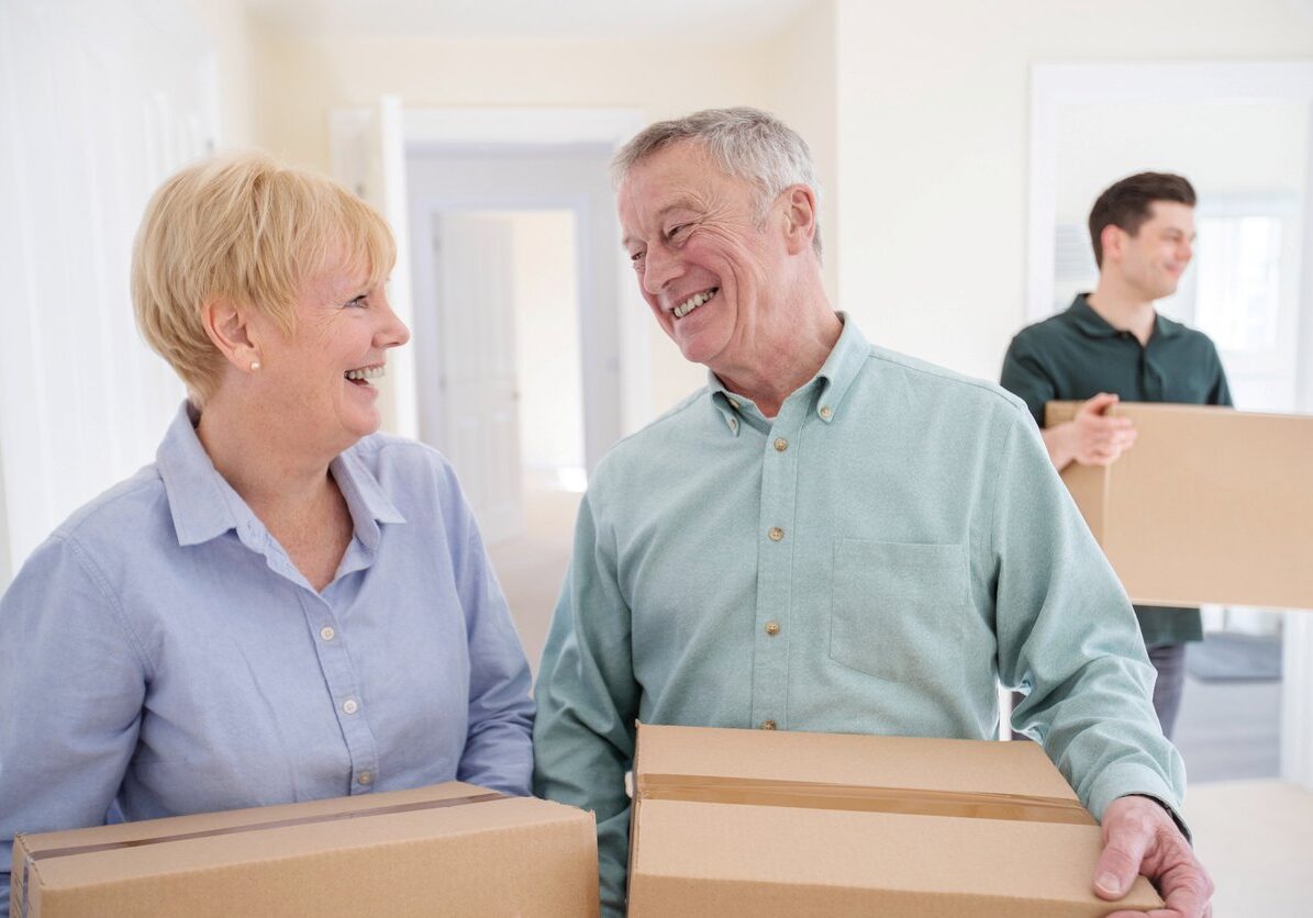 A couple holding moving boxes with a mover working behind them.