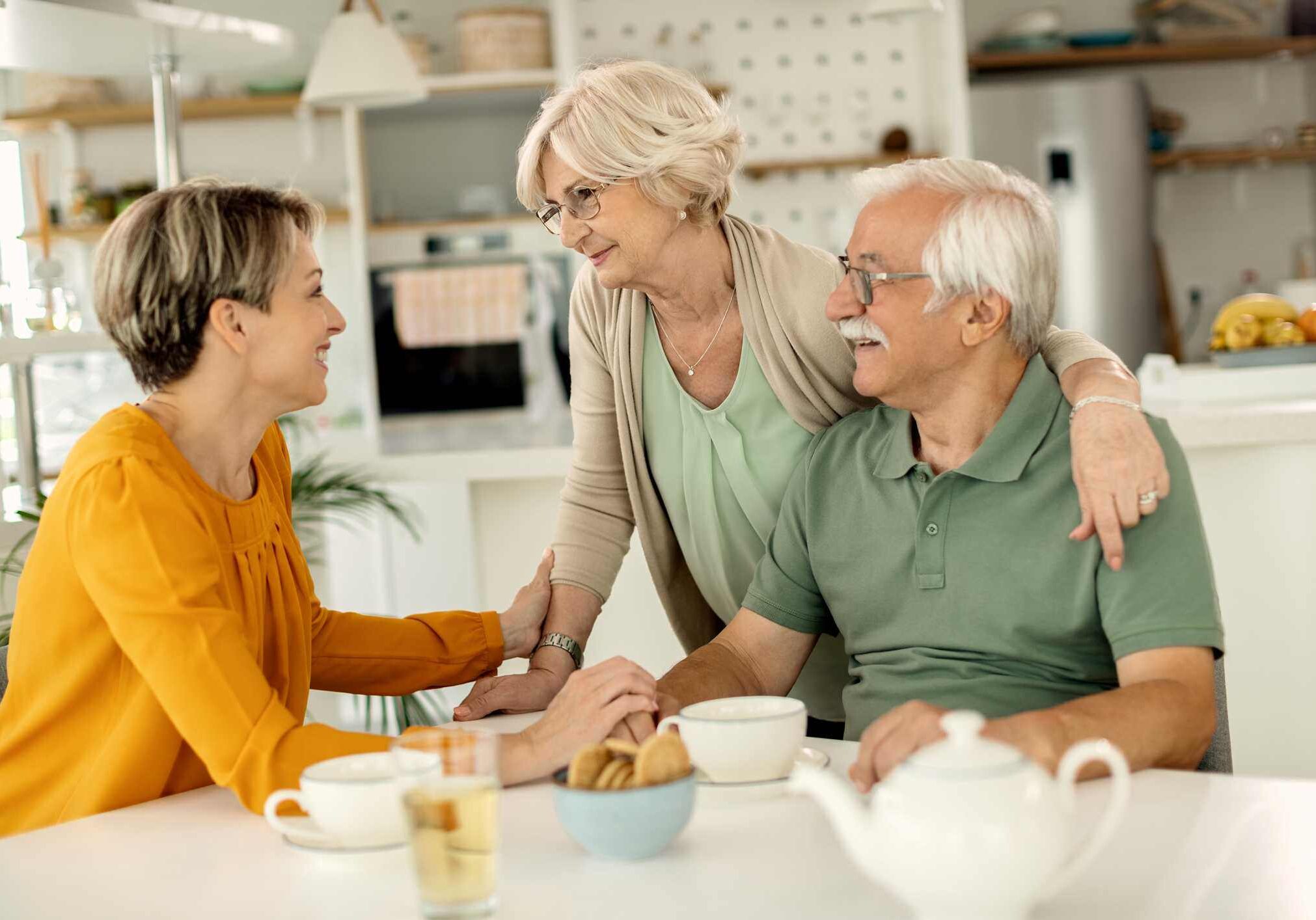 A woman sits happily at the kitchen table with her elderly parents.