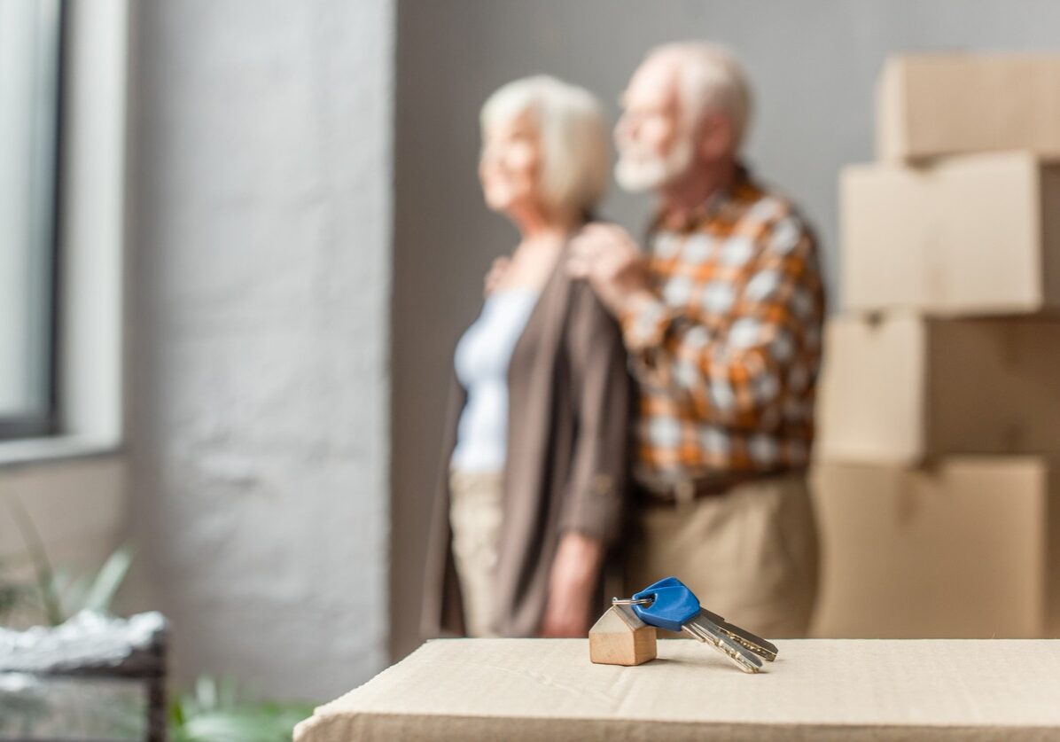 A set of keys on a shipping box with an elderly couple in the background.