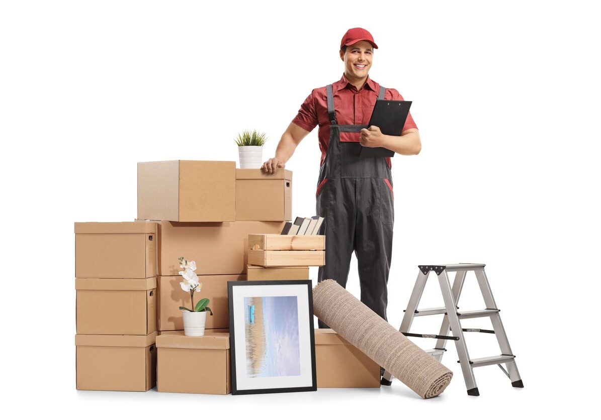 Moving manager stands around cardboard boxes and moving equipment.