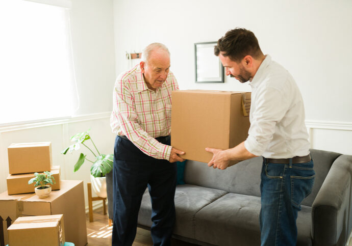 Young man carrying boxes and helping his elderly caucasian father to move to a new apartment
