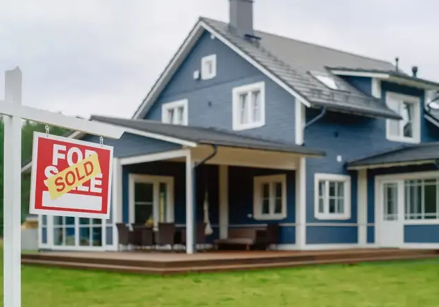Red Property Sold Sign in a Garden in Front of a Big Blue Stylish House with Traditional Architecture. Hot Housing Market Concept with Residential Home in the Suburbs.