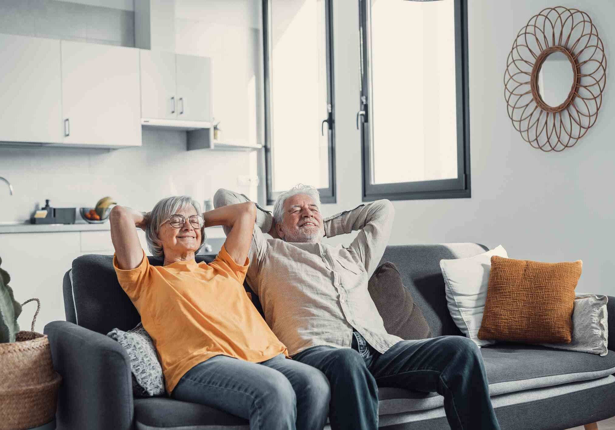 Peaceful middle aged man and woman with closed eyes relaxing on comfortable couch at home, mature family daydreaming together, grey haired wife and husband resting with hands behind head, breathing