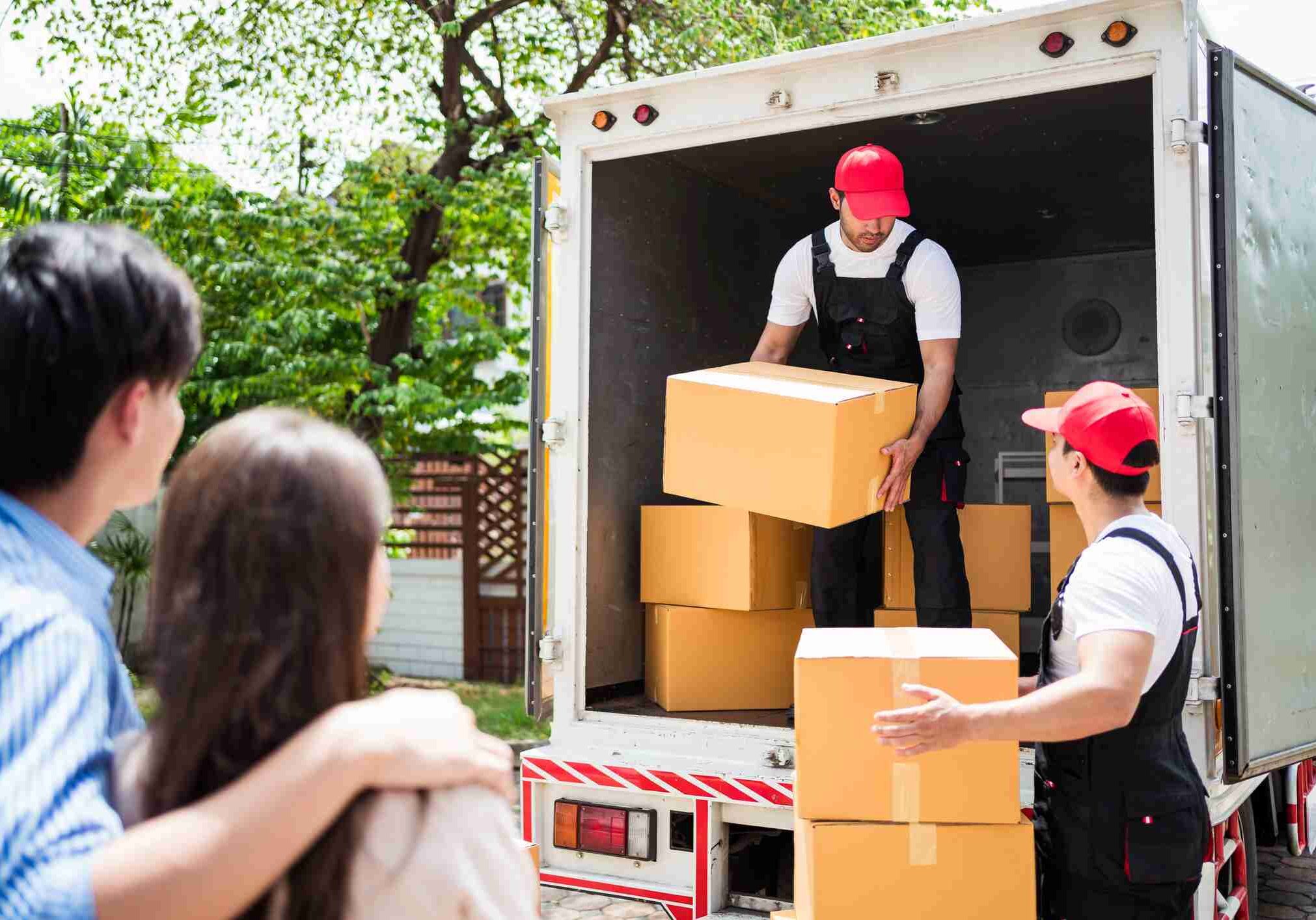 iStock-1693243234 Asian and Caucasian workers in uniform unloading cardboard boxes from the truck. Delivery men unloading boxes and check the checklist with their coworkers. Professional delivery and moving service.