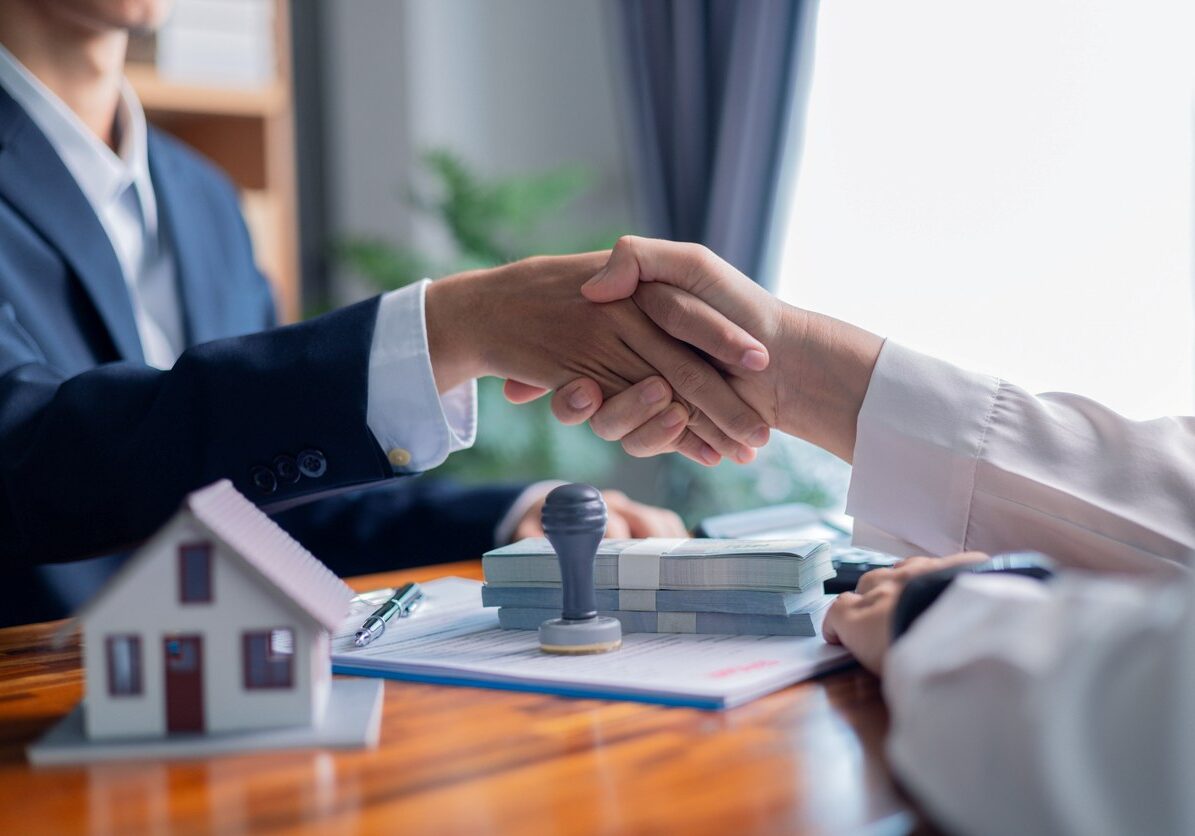 Two people shake hands over property contracts.