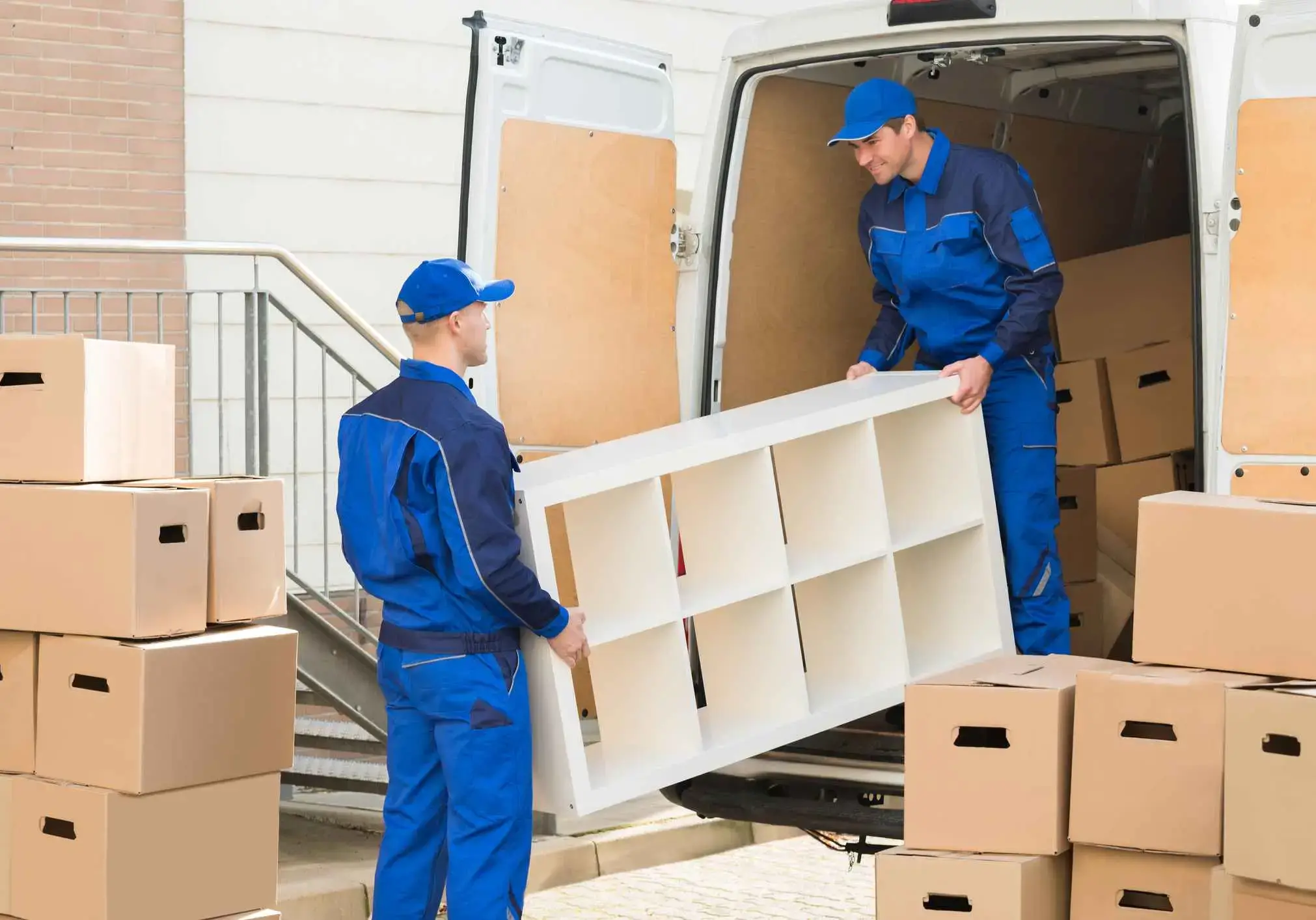 Young male movers unloading furniture and cardboard boxes from truck on street
